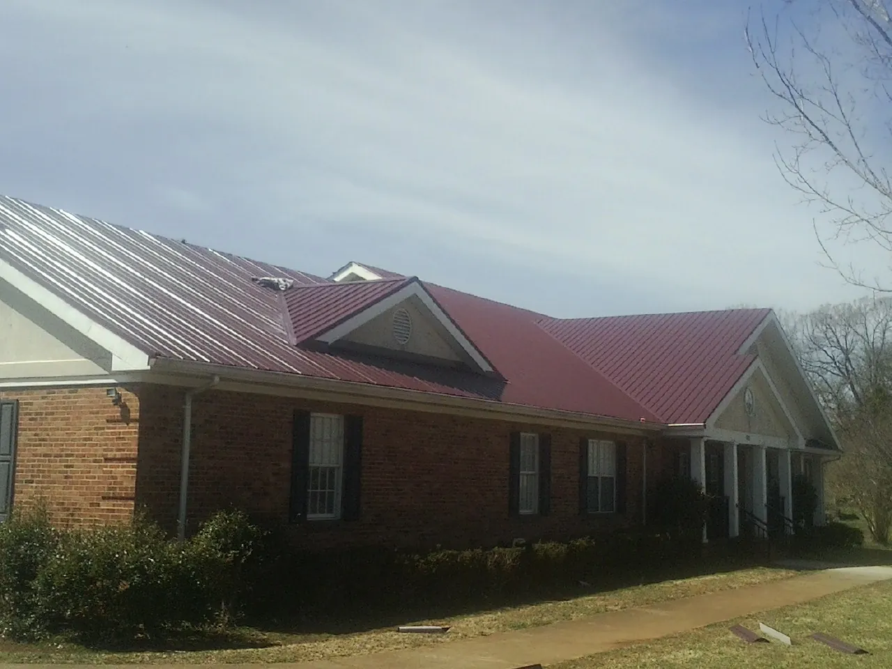 Red metal roof with gabled entries on a long brick building, from a Hail Damage Roof Repair job in Mineville