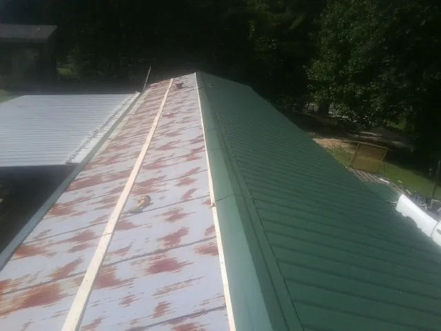 Old rusted panels beside newly installed green metal roofing — Wind Damage Roof Repair by Roofing Brothers in Mineville