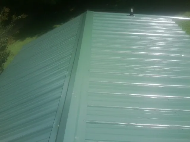 New green metal panels meeting at the ridge of a roof — Flat Roof Repair work by our crew in Mineville