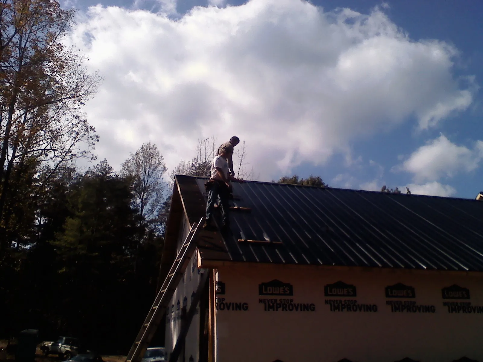 Roofer fastening dark metal panels high against a cloudy sky, from a Roof Inspection job in Mineville