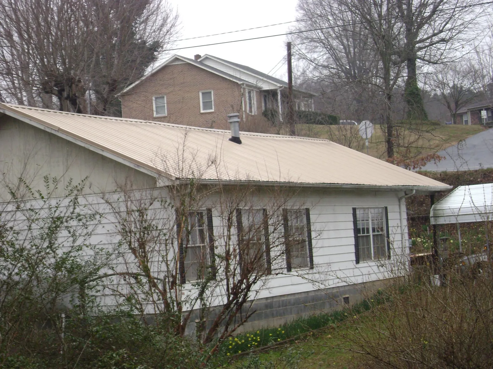 Tan metal roof on a white sided house set into a hillside — Commercial Roofing by Roofing Brothers in Mineville